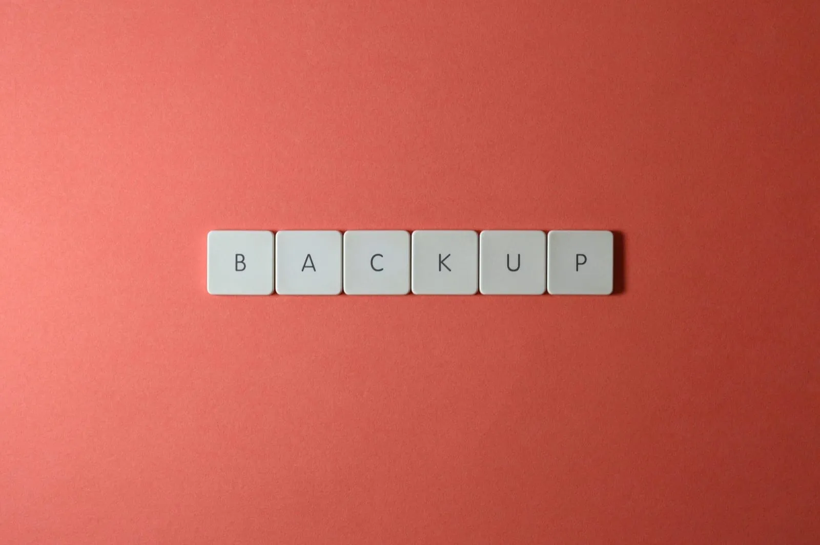 Free Close-up of keyboard keys spelling 'BACKUP' placed on a coral-colored surface. Stock Photo